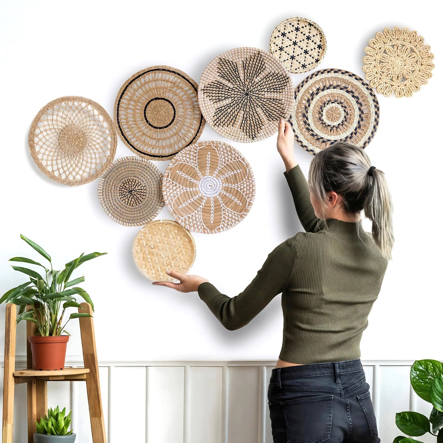 Woman decorating a wall with Boho Wall Basket Decor - Set of 9 Woven Wall Baskets for a stylish ambiance.